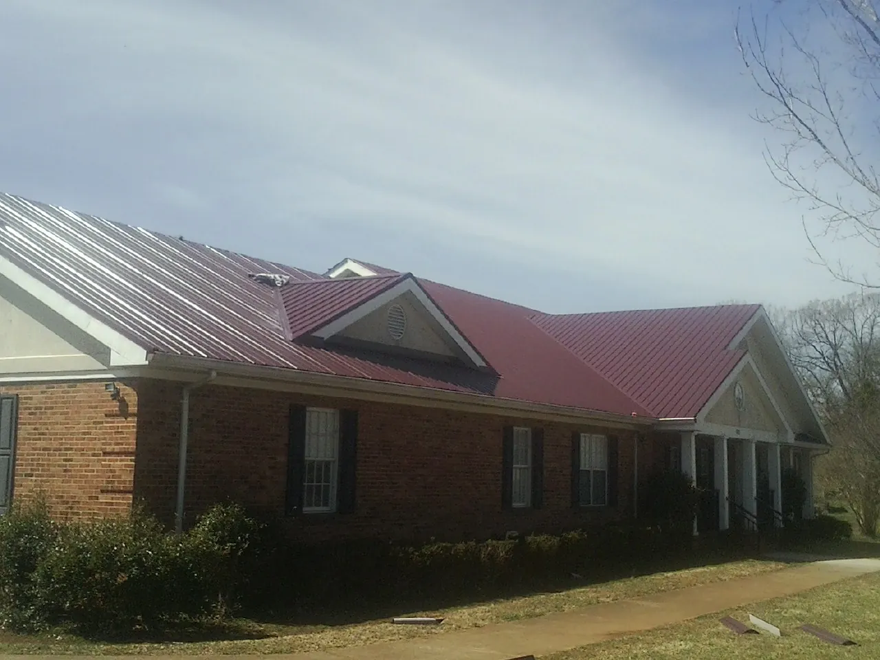 Red metal roof with gabled entries on a long brick building, from a Hail Damage Roof Repair job in Amargosa Valley