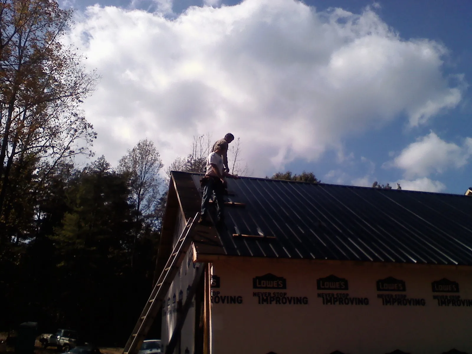 Roofer fastening dark metal panels high against a cloudy sky, from a Roof Inspection job in Amargosa Valley
